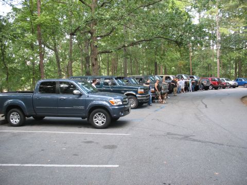 1995 Ford C-350 (Centurion Conversions) - A row of vehicles are parked in a lot, with a wooded area behind them.