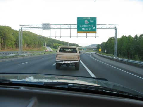 1995 Ford C-350 (Centurion Conversions) - Rear view of a tan Ford Bronco on the highway, approaching an exit for Cartersville Main St.