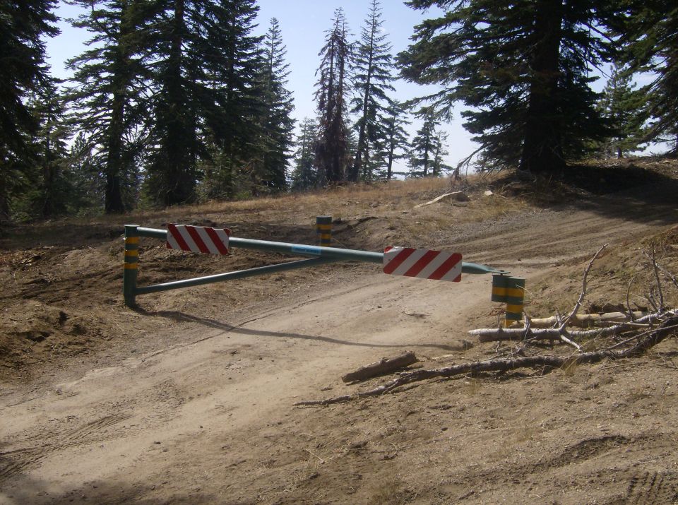 Barrier gate with red and white striped signs on a dirt road in a wooded area