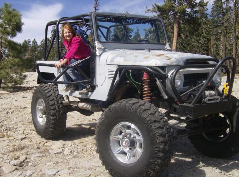 1986 Ford Bronco - A modified off-road vehicle with a prominent roll cage and oversized tires sits on a rocky terrain.