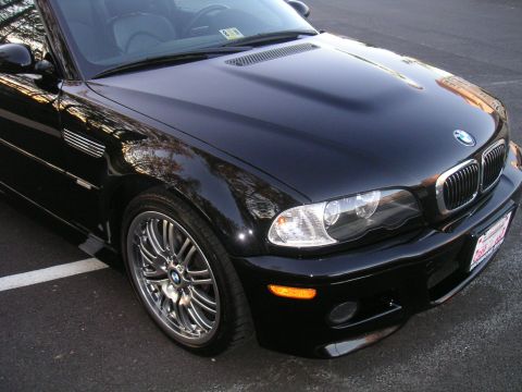 2002 BMW M3 - A black BMW M3 convertible is parked on asphalt, with reflections of trees in its paint.
