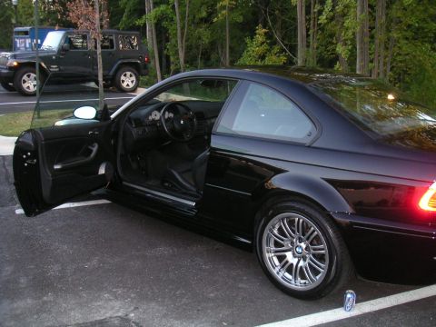 2002 BMW M3 - A black 2002 BMW M3 coupe is parked with the driver's door open, revealing the interior. Another vehicle is visible in the background.
