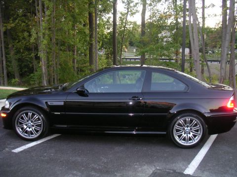 2002 BMW M3 - Side profile of a black 2002 BMW M3 coupe, captured in a parking lot with trees in the background.