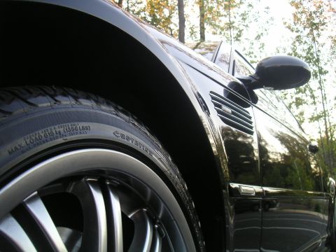 2002 BMW M3 - A low-angle shot focuses on the wheel well and side details of a shiny black car.