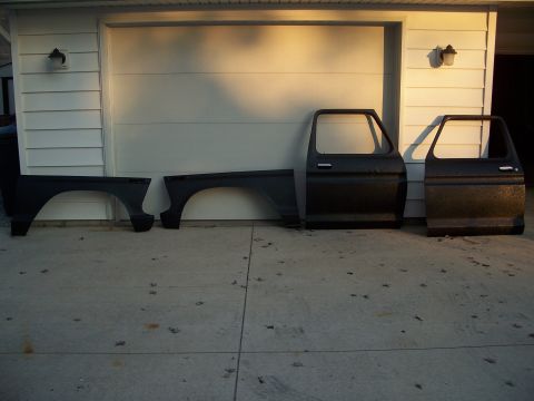 1979 Ford F-150 - Truck fender and doors are displayed on a concrete surface in front of a garage door.