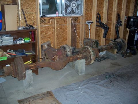 1979 Ford F-150 - Two heavily rusted truck axles are stored on concrete blocks inside a garage, with various tools and parts visible in the background.