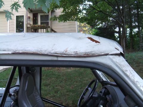 1995 Ford Bronco - The interior of an old SUV is visible, with a roll cage and a damaged, rusty roof.