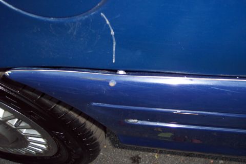 2001 Ford Crown Victoria - The side of a blue vehicle shows damage, including a noticeable scratch and a dent above the wheel well.