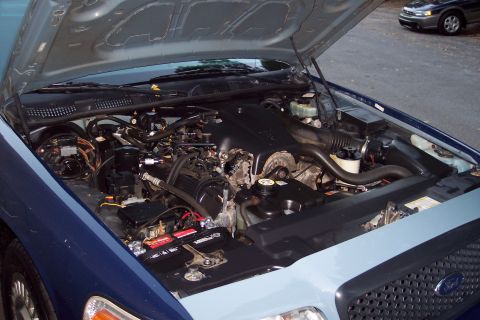 2001 Ford Crown Victoria - The engine bay of a 2001 Ford Crown Victoria is shown with the hood open. Another vehicle is visible in the background.