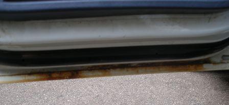 2000 Ford Crown Victoria - The lower door sill of a white vehicle shows significant rust damage.