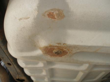 2000 Ford Crown Victoria - Close-up view of a corroded vehicle component, possibly a fuel tank or cover.