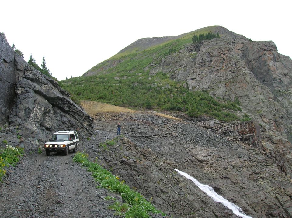 White Land Rover Discovery SUV on a rocky mountain shelf road with alpine peaks