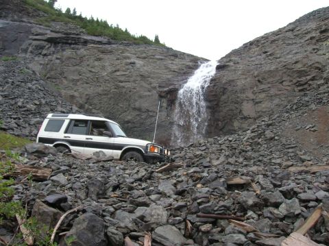 1999 Land Rover Discovery II - A white 1999 Land Rover Discovery II traverses a challenging rocky landscape with a waterfall cascading down a cliff in the background.