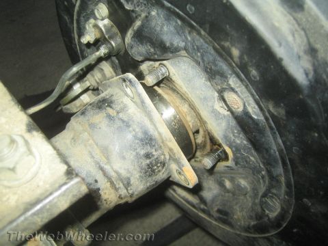 1987 Suzuki Samurai - Greasy underside view of a rear axle showing leaf spring U-bolts, perch and brake backing plate. TheWebWheeler.com.