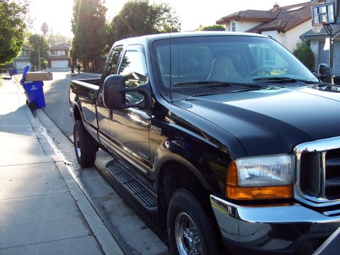2000 Ford F-250 - A black Ford F-250 pickup truck is parked curbside on a sunny day, with residential homes in the background.
