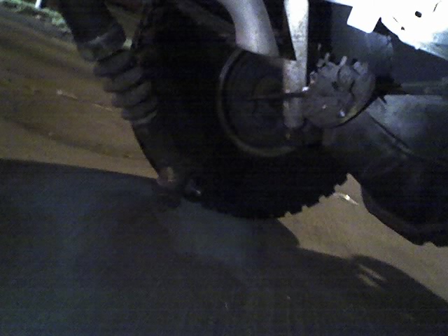Close-up of a dark tire and suspension parts, with a Supermotors logo in the corner