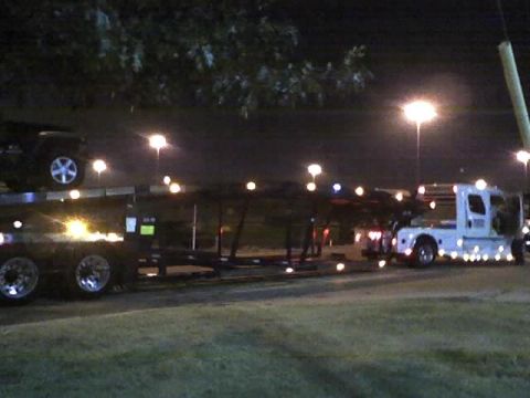 1992 Ford Bronco - A car carrier truck transports a dark SUV at night.