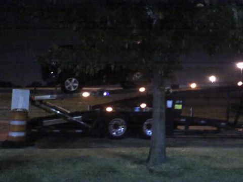 1992 Ford Bronco - Dark SUV and a car trailer are visible at night. The SUV's year is not discernible.