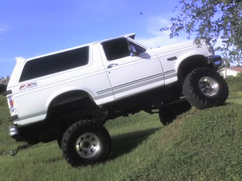 1995 Ford Bronco - This lifted SUV is shown on a grassy hill under a clear blue sky.