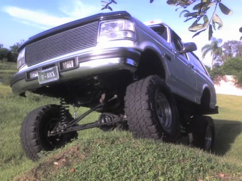 1995 Ford Bronco - This lifted Ford Bronco has a custom grille and large off-road tires, seen from a low angle on a grassy incline.