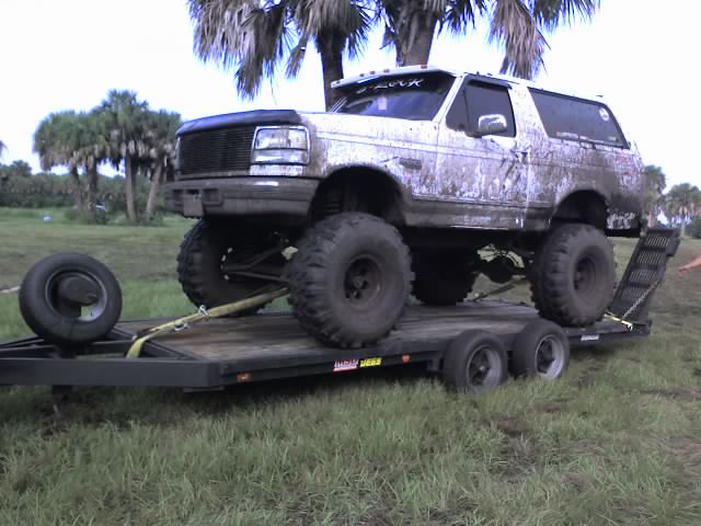 1995 Ford Bronco with large tires on a flatbed trailer, covered in mud