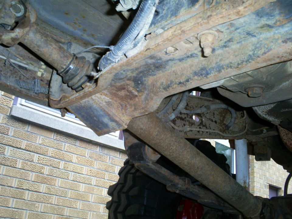 Underside of a truck showing rusty frame, driveshaft, and suspension components