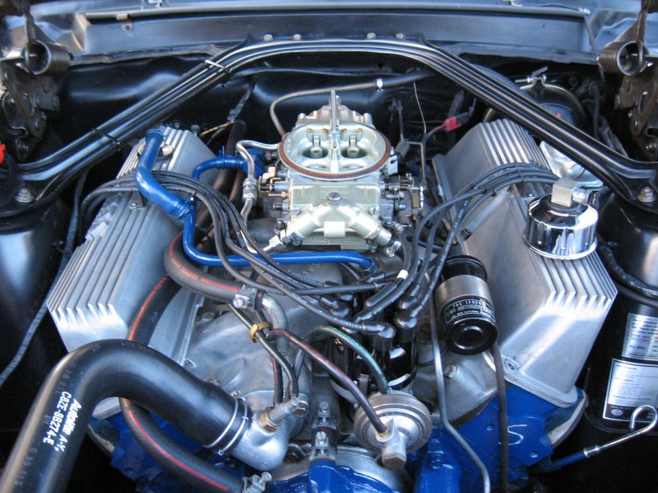 Close-up of a V8 engine, showing dual carburetors, aluminum valve covers, and blue engine components
