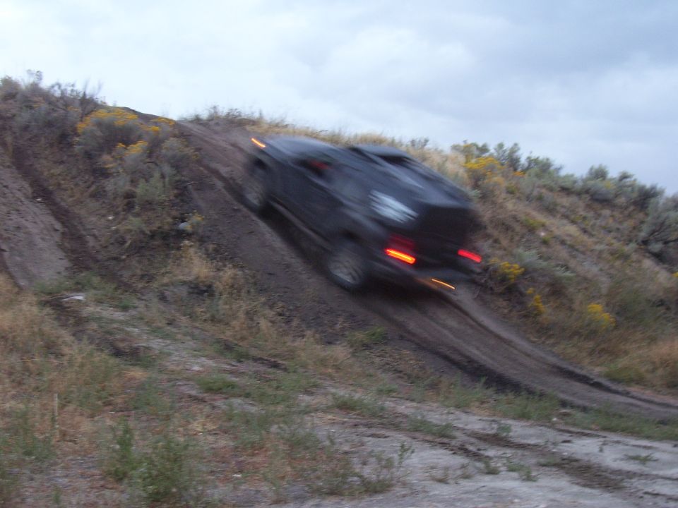 Dark SUV climbing a steep dirt trail off-road, rear view, taillights on, motion-blurred