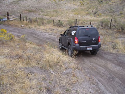 1990 Ford Bronco - A black Nissan Xterra navigates a dusty, off-road path with sparse vegetation and a rustic fence line.