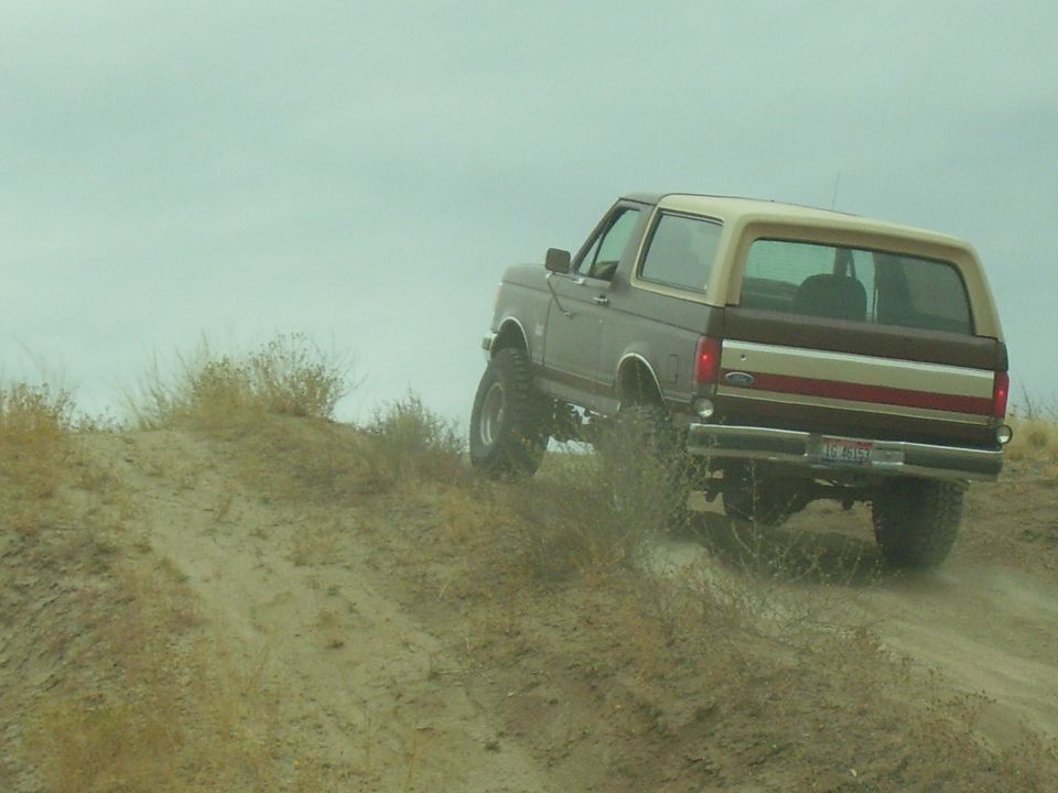1990 Ford Bronco driving up a sandy hill, rear view