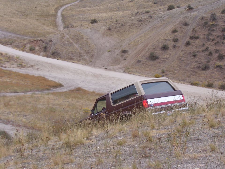 Maroon 1990 Ford Bronco with tan top on a dirt hill, rear quarter view