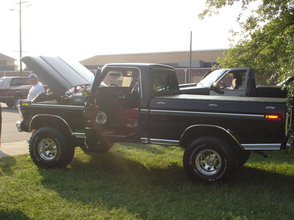 Black 1979 Ford F-350 pickup truck with hood and driver door open, parked on grass