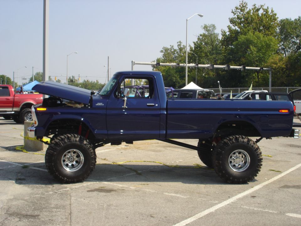 Blue lifted pickup truck with hood open, parked next to a red pickup truck