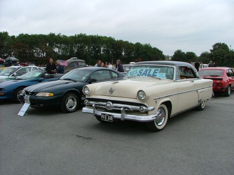 2001 Ford Fiesta - Cream 1950s coupe for sale, parked next to a dark green Ford Mustang and a red hatchback.