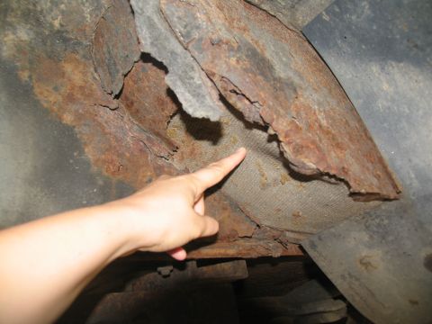 1995 Ford C-350 (Centurion Conversions) - Severe rust damage is visible on the undercarriage of a vehicle, with a hand pointing to a torn fabric liner.