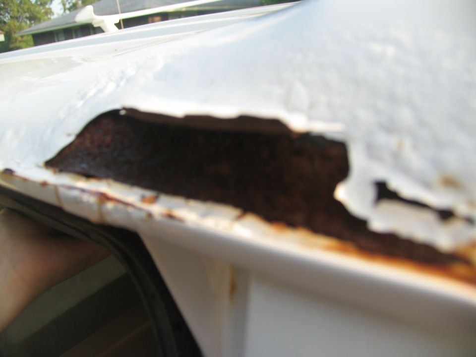 Close-up of rust damage and peeling paint on the edge of a white vehicle's roof