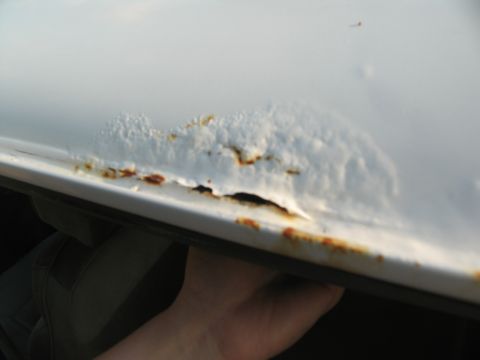 1995 Ford C-350 (Centurion Conversions) - Close-up of severe rust damage on the edge of a white vehicle's roof, revealing a hole where paint has flaked away.