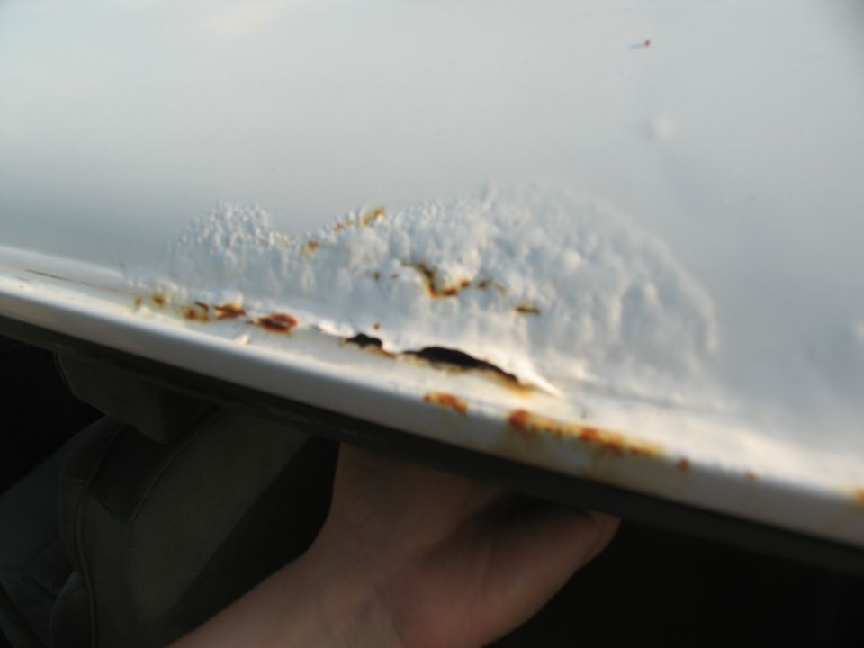 White vehicle roof edge with extensive rust and peeling paint, showing a hole