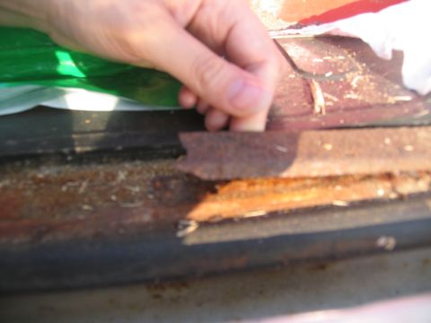 1995 Ford C-350 (Centurion Conversions) - Close-up of heavily rusted metal trim on a vehicle, with a hand pulling at a loose section.