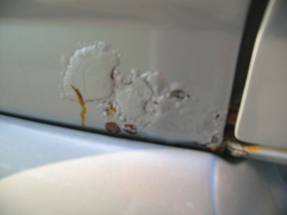 Close-up of rust and paint bubbles on a light-colored vehicle body panel