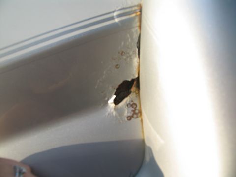 1995 Ford C-350 (Centurion Conversions) - A close-up view shows significant rust and a hole on a silver vehicle panel.