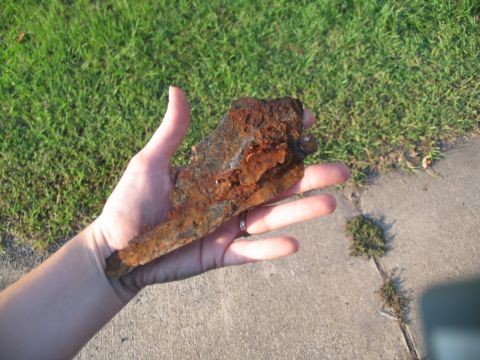 1995 Ford C-350 (Centurion Conversions) - A heavily rusted metal fragment is held in a person's hand outdoors.