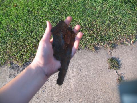 1995 Ford C-350 (Centurion Conversions) - A hand holds a piece of rusty metal. The background shows grass and a concrete path.