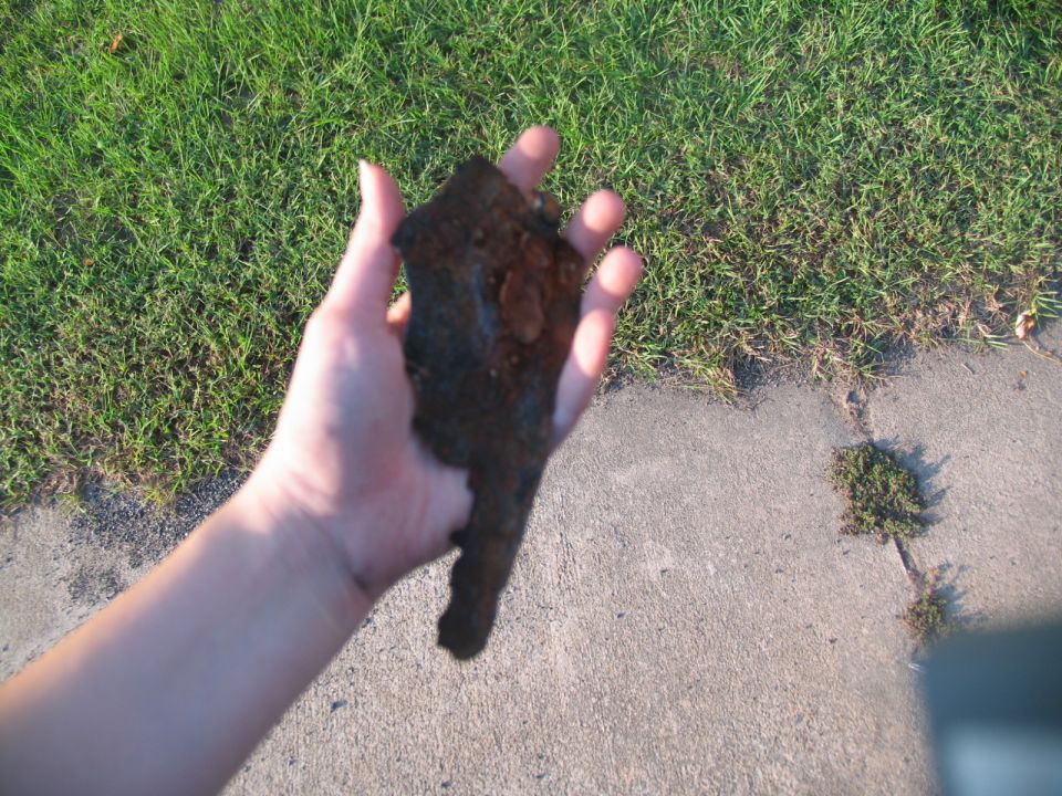 Rusty metal fragment held in a hand over concrete and grass