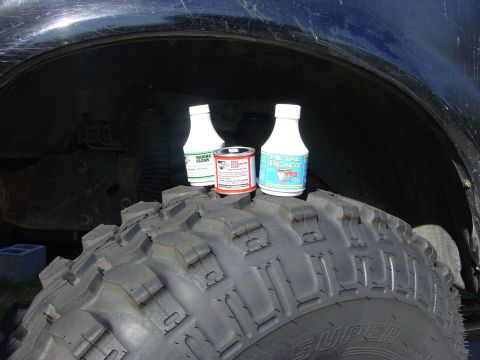 1994 Ford Bronco - Three bottles of cleaning products sit on a large tire in front of a vehicle's wheel well.