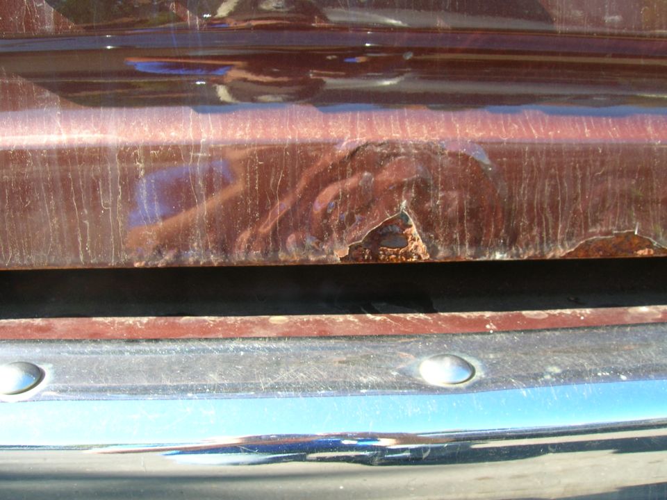 Close-up of rusted metal on a vehicle's body panel above a chrome bumper