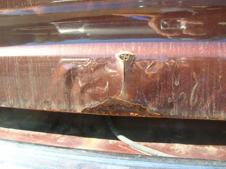 Close-up of a rusty, dented car panel with a crack and peeling paint