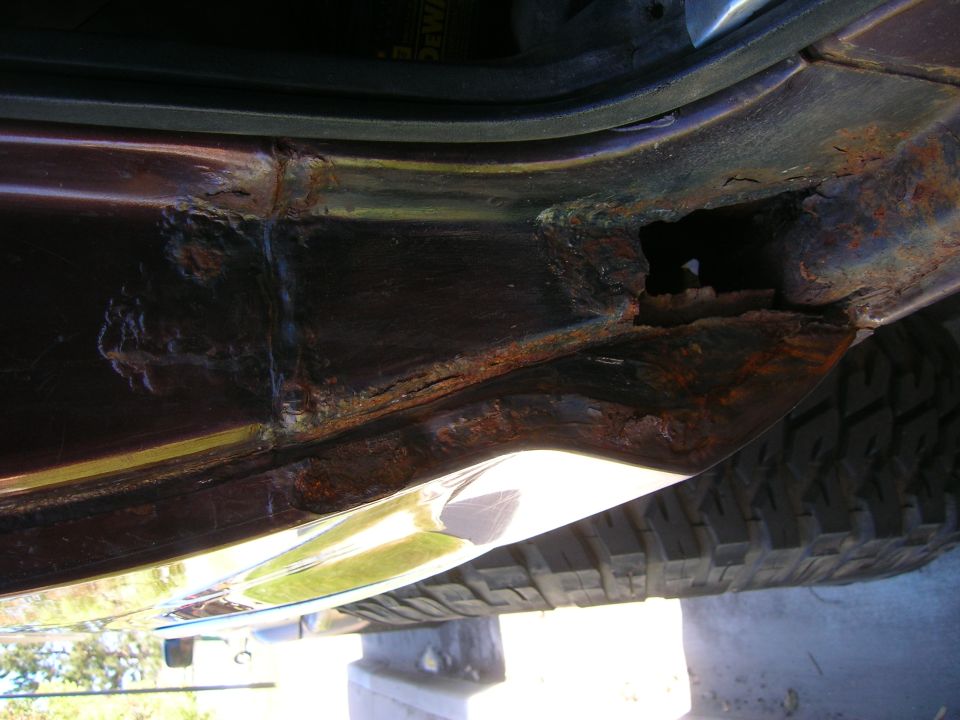 rusted rocker panel with hole, tire visible below