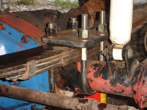 1989 Ford Bronco - Close-up of a leaf spring U-bolt and shock absorber mount on a vehicle's axle, showing signs of rust and wear.