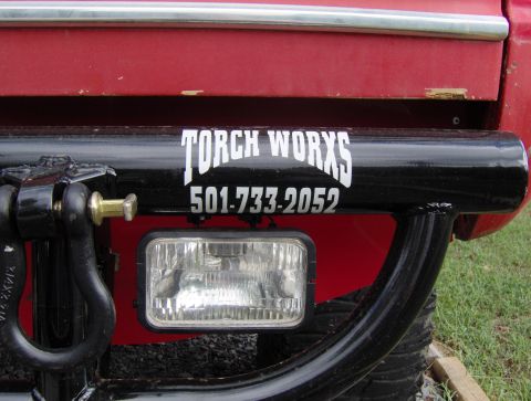 1978 Ford Bronco - A red vehicle's rear bumper is equipped with a black tubular guard, a tow hitch, and a rectangular light, displaying company contact inform…